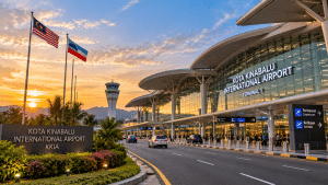 kkia - MKAZ Car Rental - MKAZ Car Rental Exterior view of Kota Kinabalu International Airport at sunset, with flagpoles, control tower, and glass terminal.